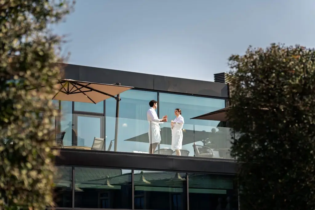 Una coppia in accappatoio sorseggia un drink sul balcone di un hotel di lusso con vista sulla città.