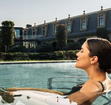 Donna rilassante in piscina termale con vista sull'hotel. Benessere e relax.