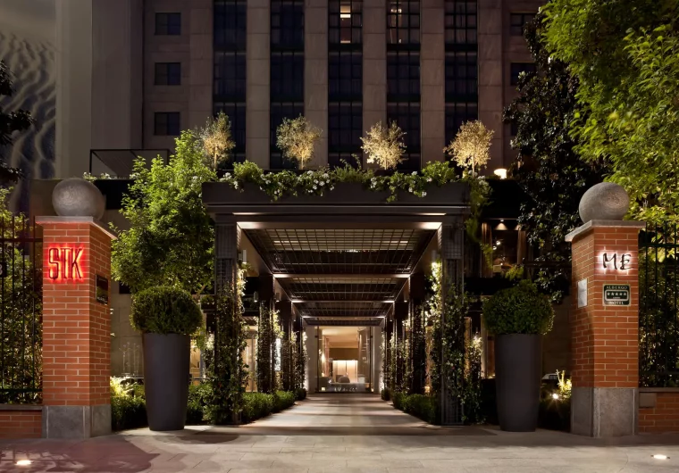 Ingresso elegante di un hotel con insegna luminosa STK e ME, circondato da vegetazione