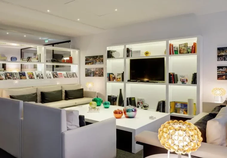Lounge moderna con divani bianchi, librerie illuminate e TV, ideale per hotel partner.