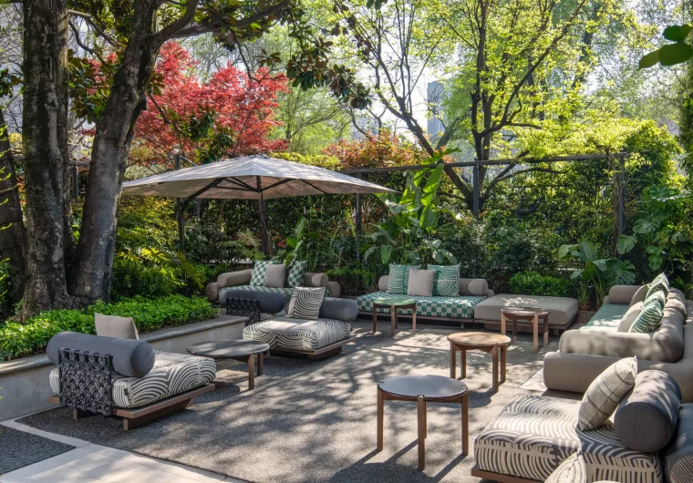 Salotto esterno moderno con divani modulari e tavolini in un giardino lussureggiante.