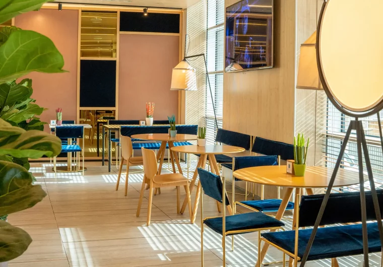 Interno di un ristorante moderno con tavoli rotondi, sedie blu e luce naturale.